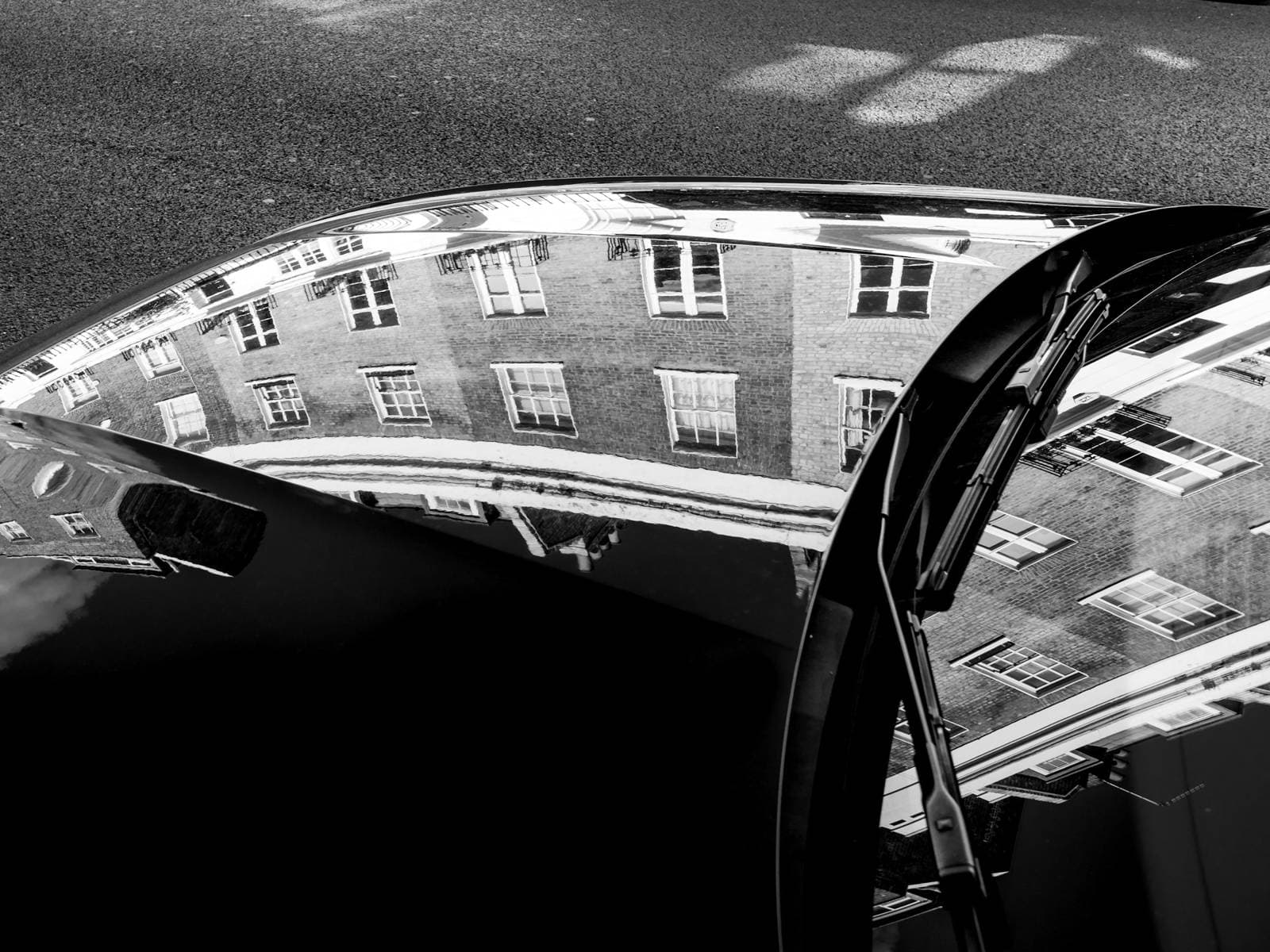 The polished bonnet of a dark car reflecting the windows of a brick building