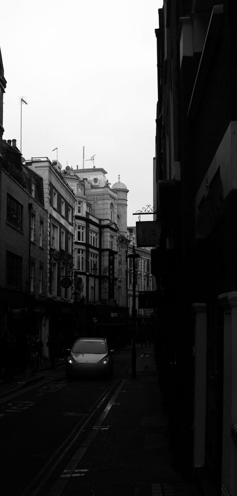 A narrow London side street between tall brick buildings, a single car approaching