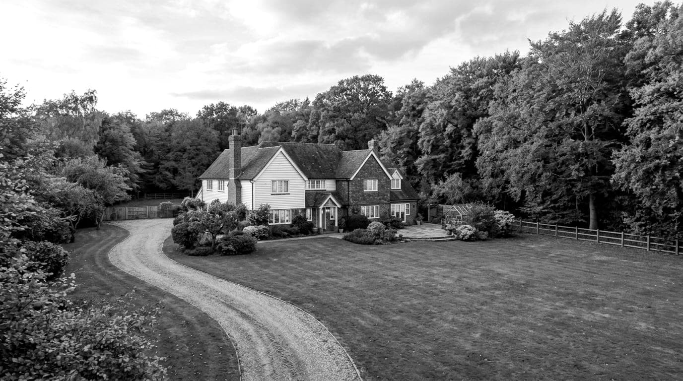 Weatherboarded house with tile hung gables at the end of a sweeping gravel drive, autumn trees crowding behind