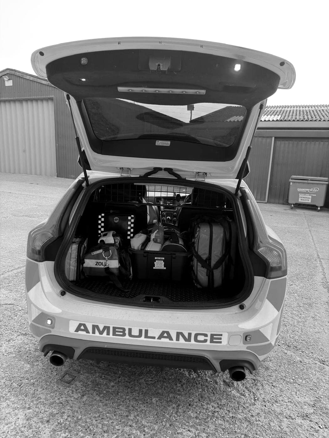 The open tailgate of a BPS ambulance car, medical bags and kit packed in the boot