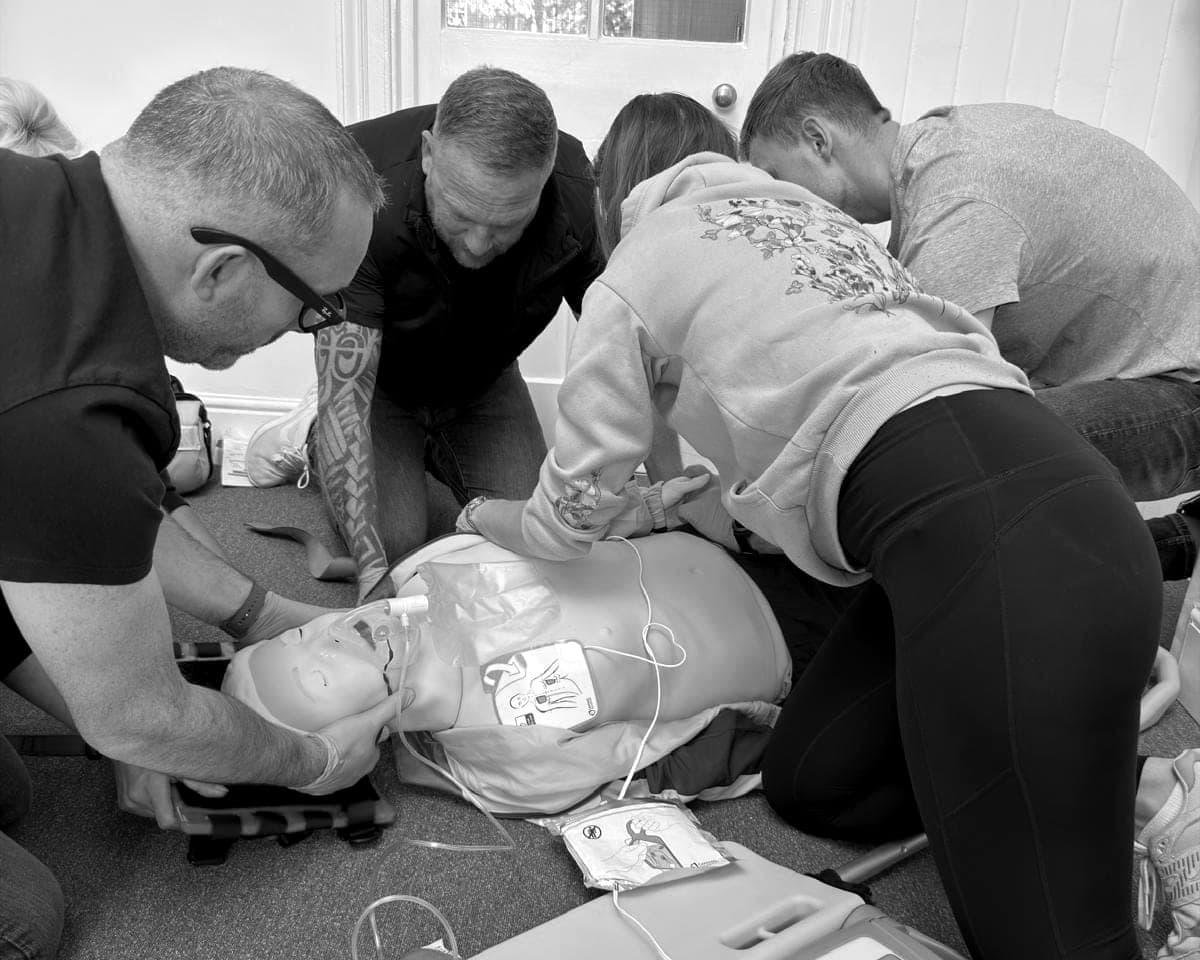 Course members practising resuscitation on a training manikin with defibrillator pads on its chest, during a BPS first aid training session