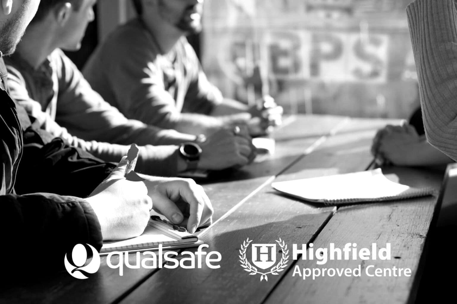 Delegates working at a table during a BPS training course, Qualsafe and Highfield marks overlaid