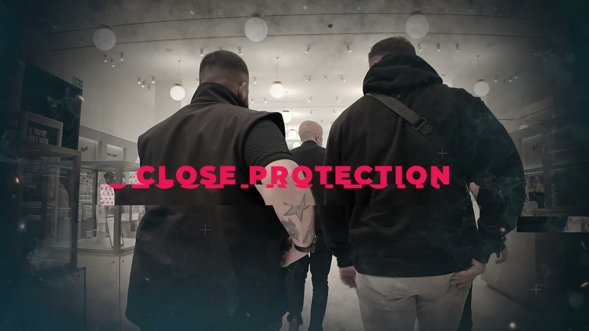 A frame from the BPS film: two team members seen from behind walking through a shopping centre, the title Close Protection across them